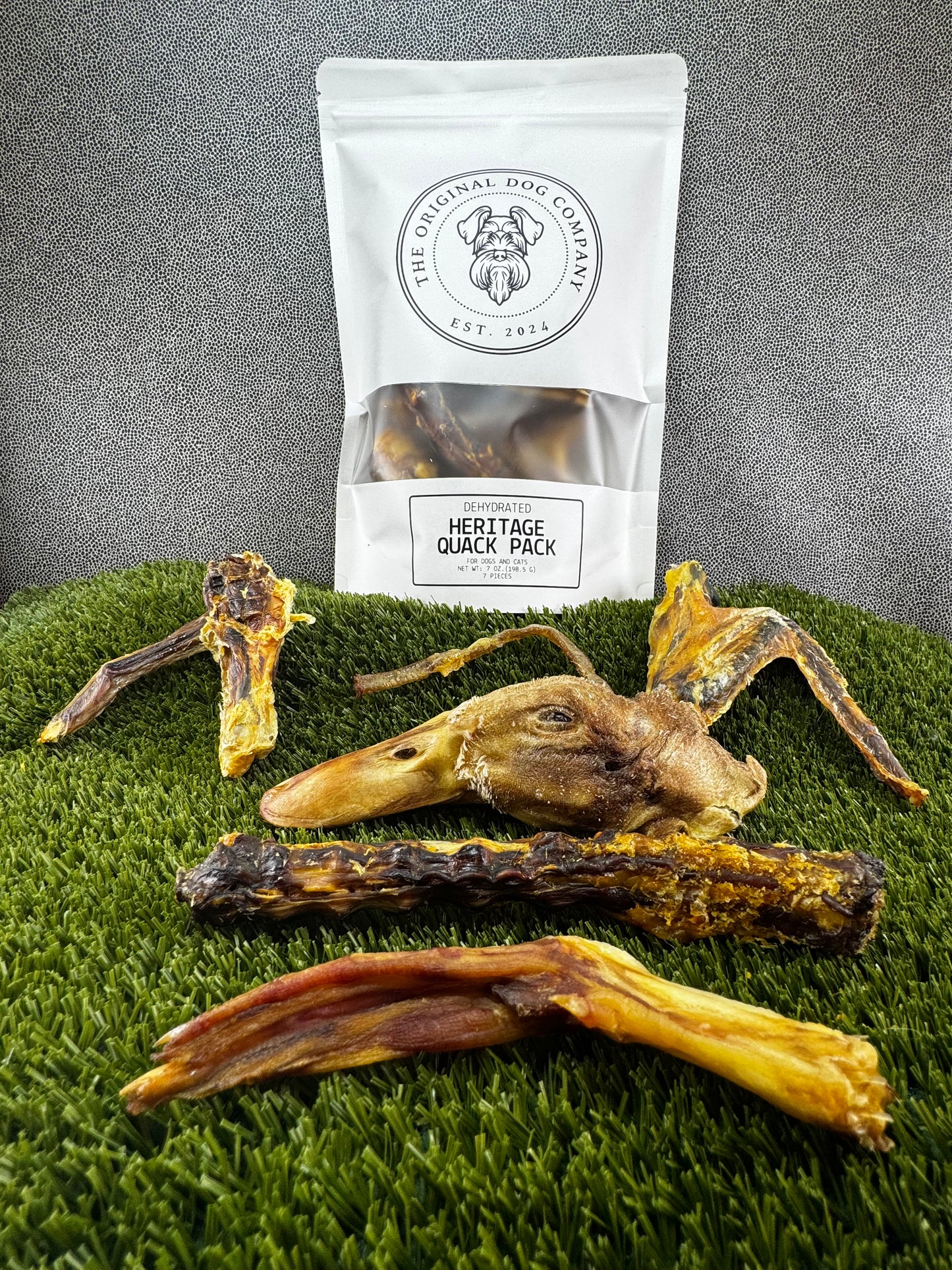 Dog chews on a grassy surface with a branded packaging bag in the background.