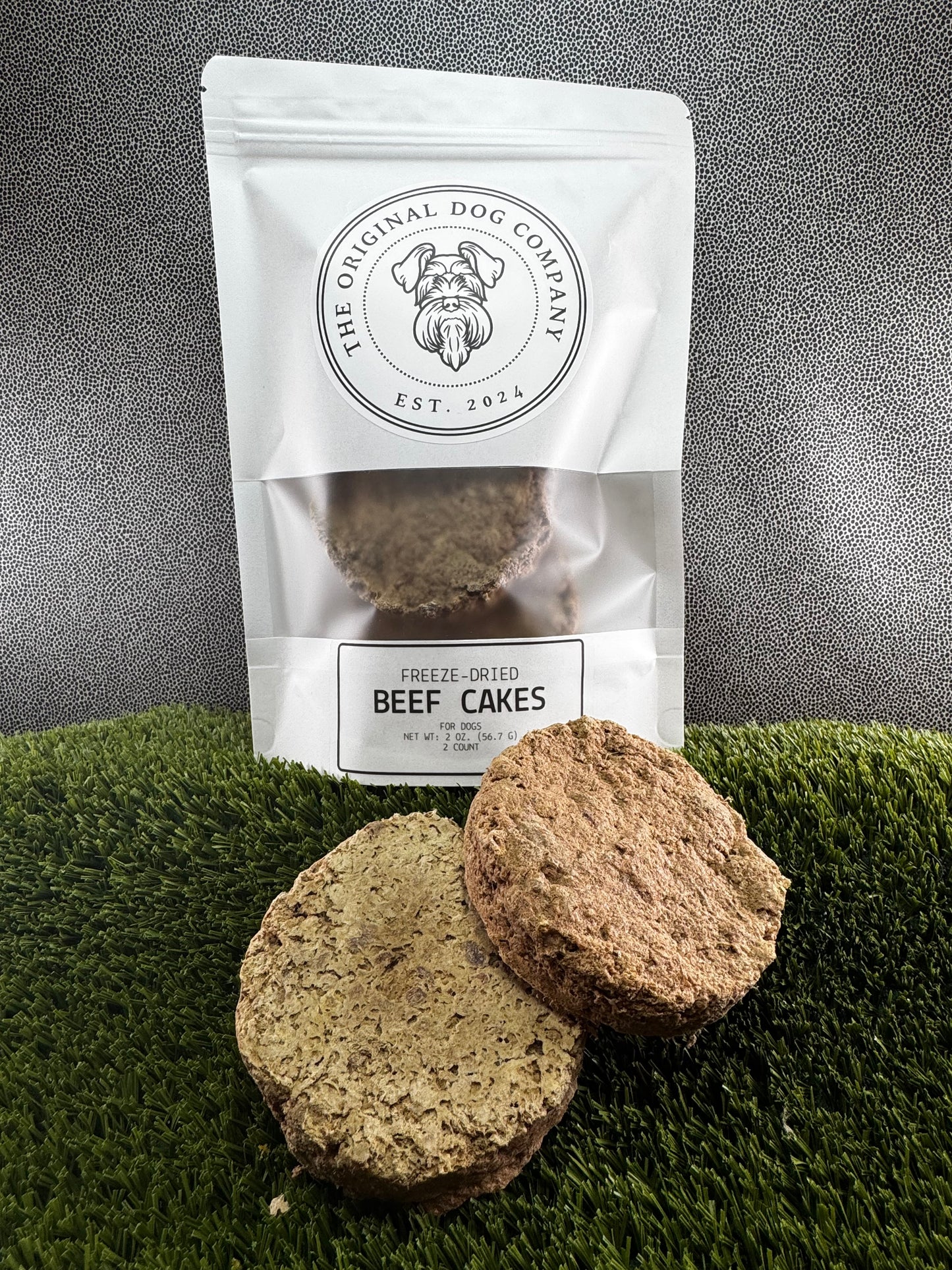 Two beef cakes treats for dogs in front of a bag labeled 'The Original Dog Company' on a grassy background.
