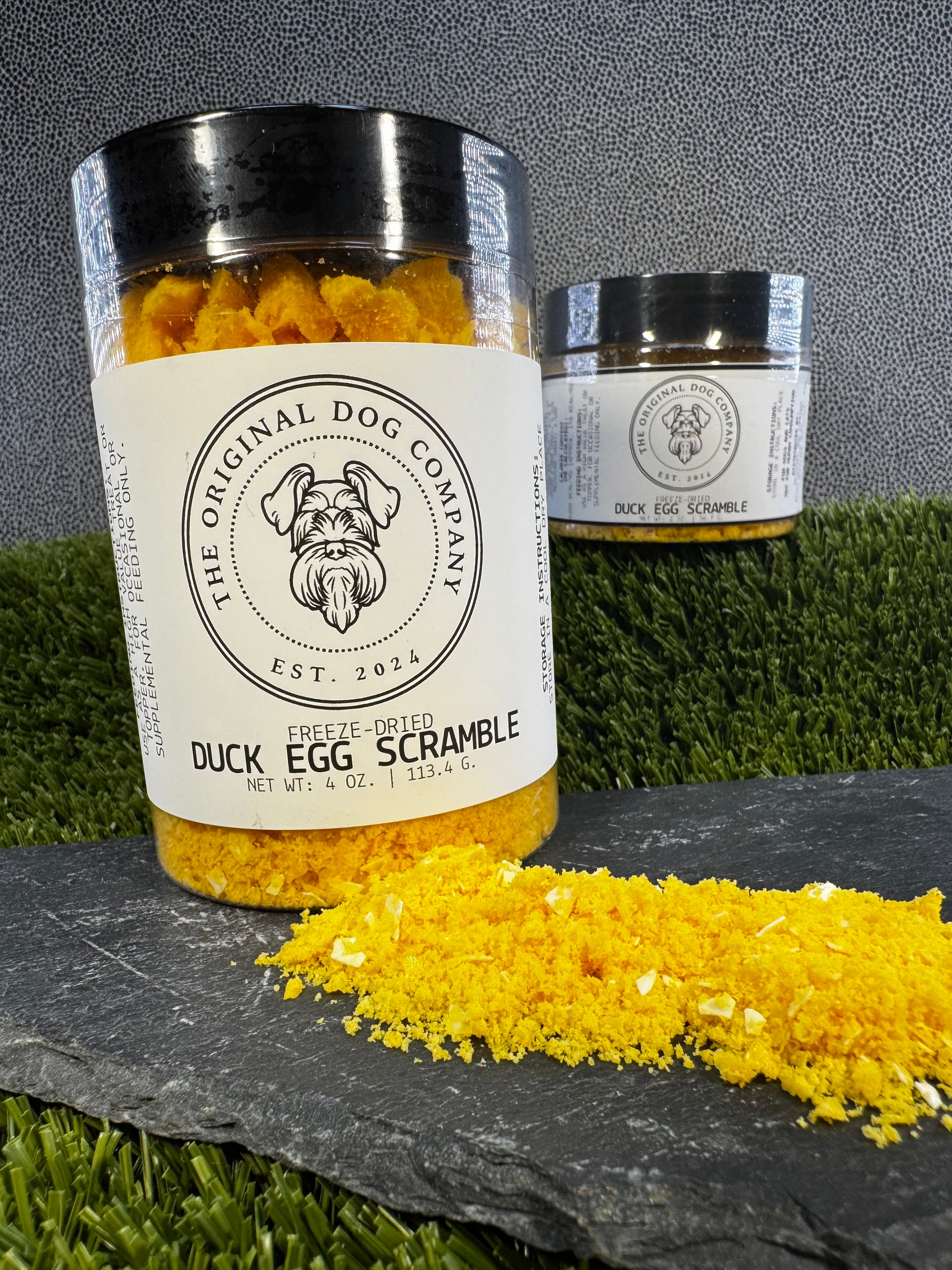 Two jars of 'Duck Egg Scramble' from The Original Dog Company on a grassy background.